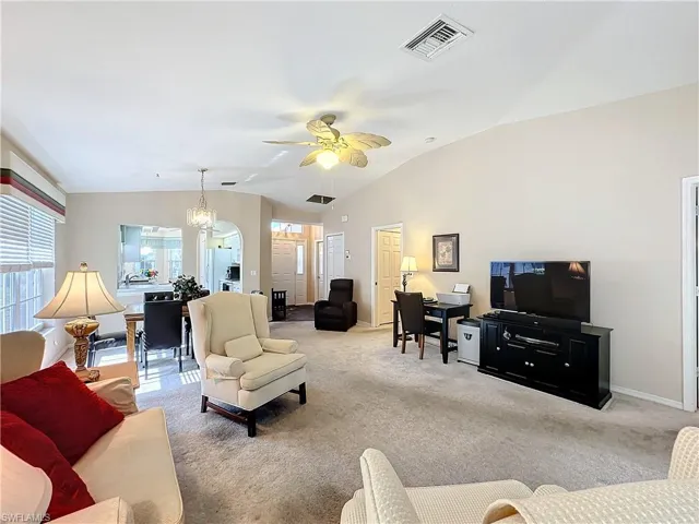 Living room with vaulted ceiling, carpet floors, and ceiling fan with notable chandelier