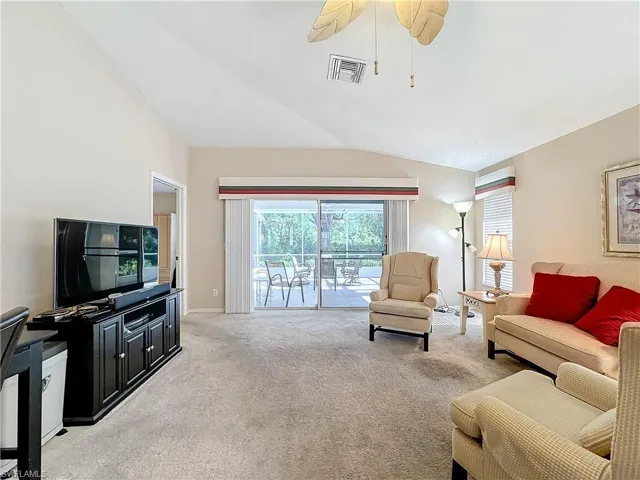 Carpeted living room featuring ceiling fan and vaulted ceiling
