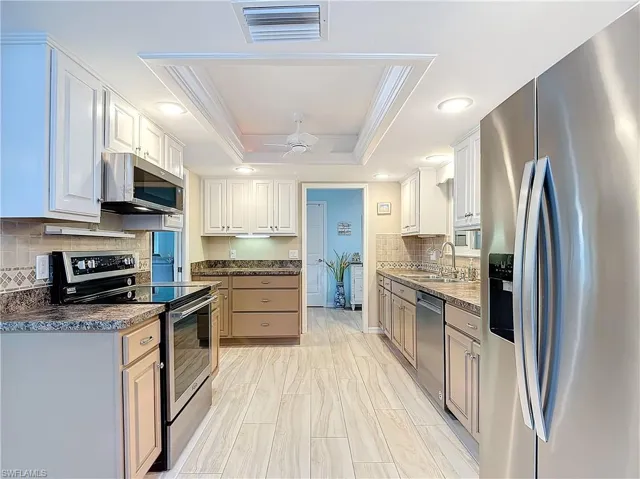 Kitchen with tile backsplash, under cabinet lighting, stainless steel appliances, and a tray ceiling.