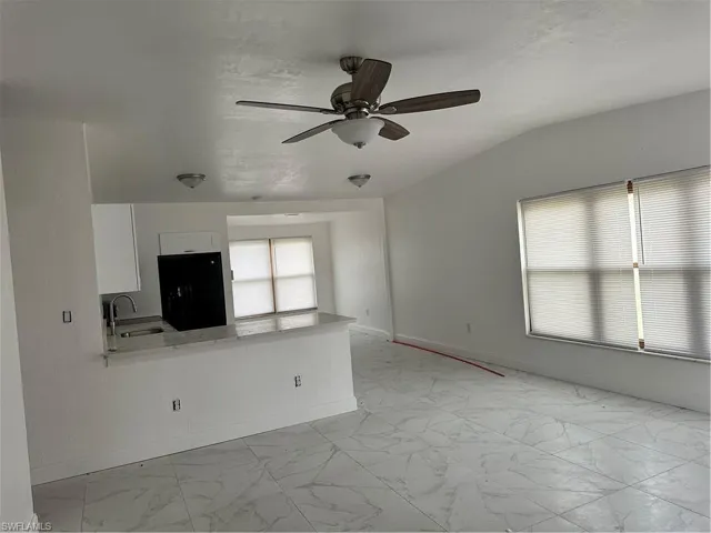 Unfurnished living room with a ceiling fan, light marble finish flooring, and vaulted ceiling