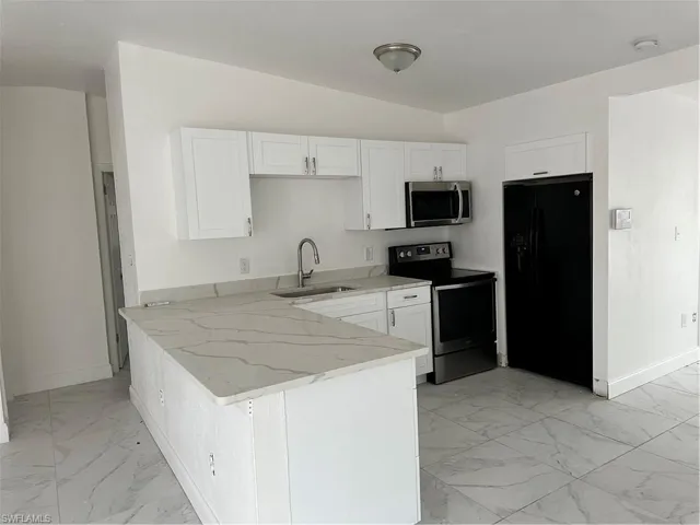 Kitchen featuring refrigerator, range, white cabinetry, a peninsula, and light marble finish flooring