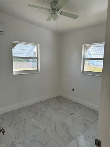 Empty room featuring a ceiling fan, healthy amount of natural light, and light marble finish flooring