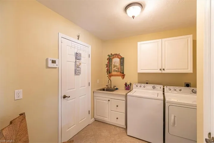 Laundry area with a utility sink, light-toned cabinetry, and tile flooring