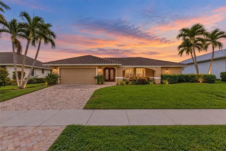 Tiled-roof residence with a paver driveway, an arched entry, mature palm trees, and established landscaping