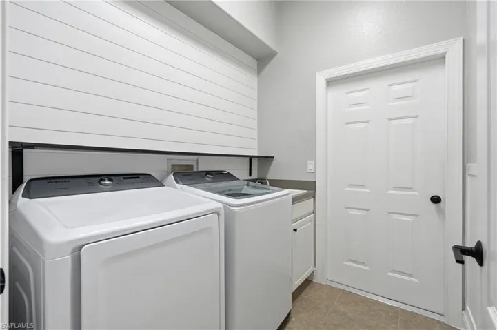 Laundry area featuring shiplap accent wall, built-in shelf, white cabinetry, dark countertop, and tile flooring