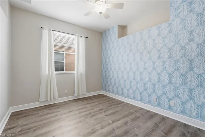 Room featuring wood-finish flooring, a contemporary ceiling fan, and a patterned accent wall
