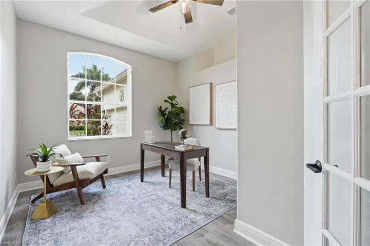 Room featuring an arched window, wood-finish flooring, and a tray ceiling with a ceiling fan