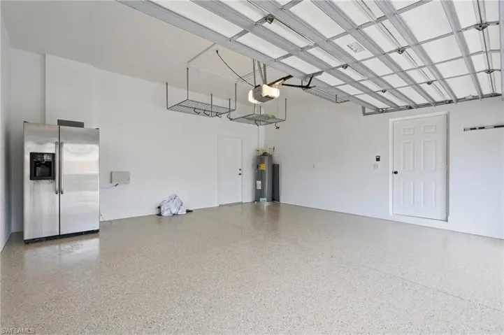 Spacious garage with light-toned epoxy flooring, white painted walls, exposed ceiling joists, and overhead storage racks