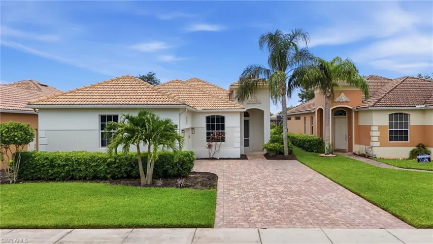 Mediterranean-style residence featuring a tile roof, light-colored stucco exterior, and a paver driveway