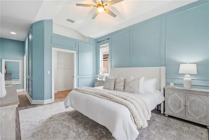 Vaulted ceiling room featuring decorative wall paneling and a ceiling fan with integrated lighting
