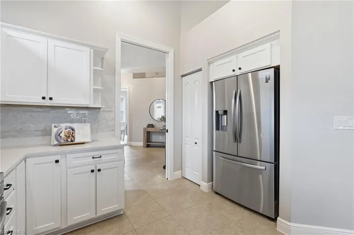 Kitchen featuring white cabinetry with black hardware, light-toned countertops, and a herringbone pattern tile backsplash