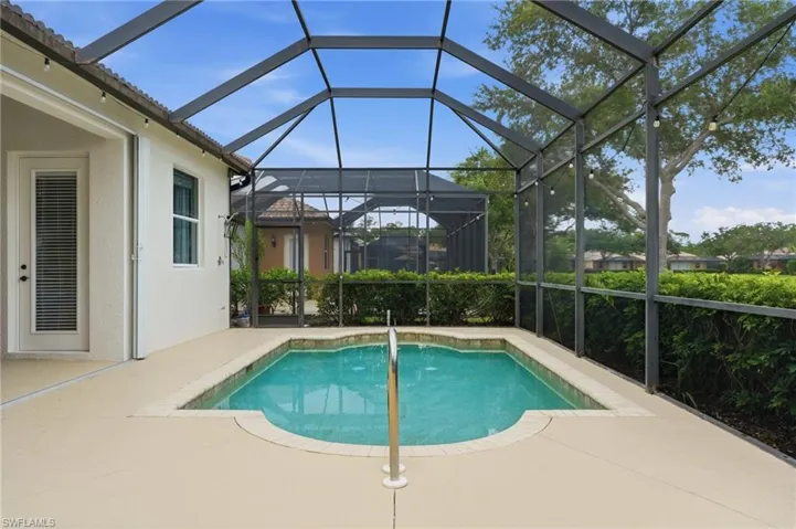 Screened pool area featuring a custom-shaped inground pool with a metal handrail, paver coping, and ample deck space