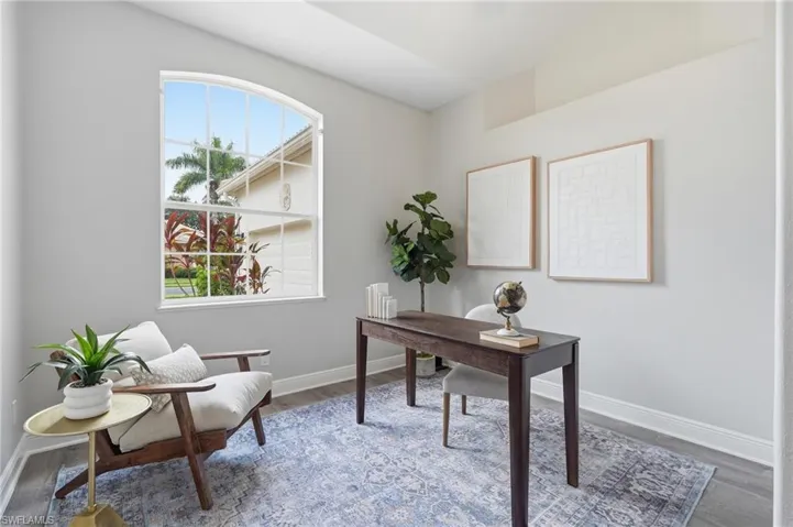 Arched window offering natural light, light gray walls, wood-finish flooring, white baseboards, and overhead architectural detailing