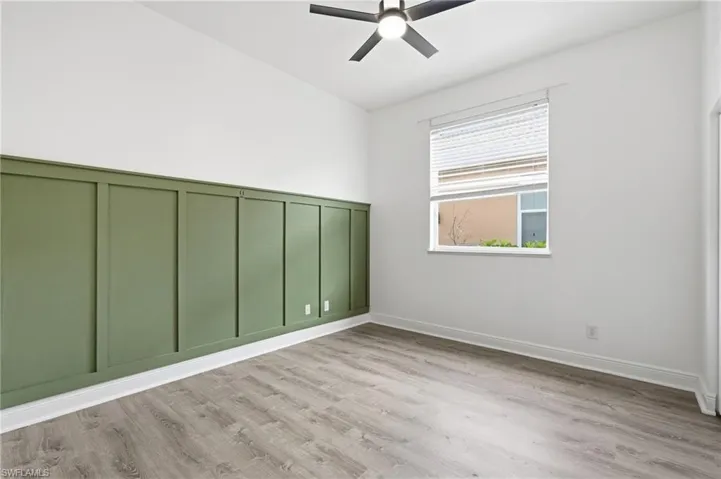 Room featuring a decorative green wainscoting wall panel, wood-finish flooring, and a ceiling fan