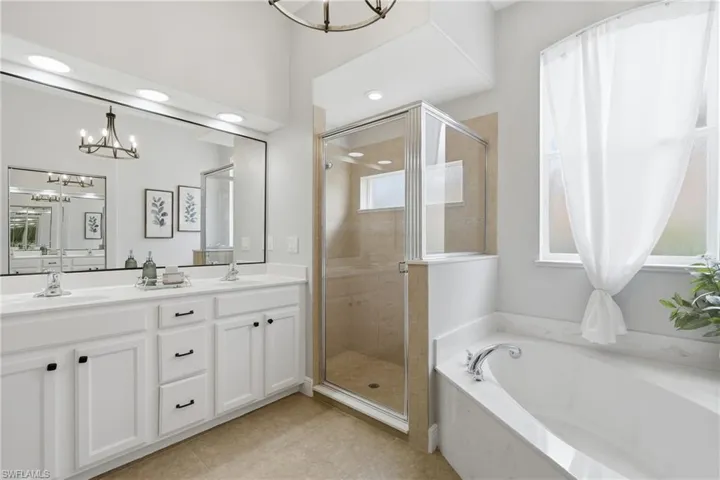 Bathroom featuring a dual vanity with white cabinetry, a glass-enclosed shower, and a built-in soaking tub
