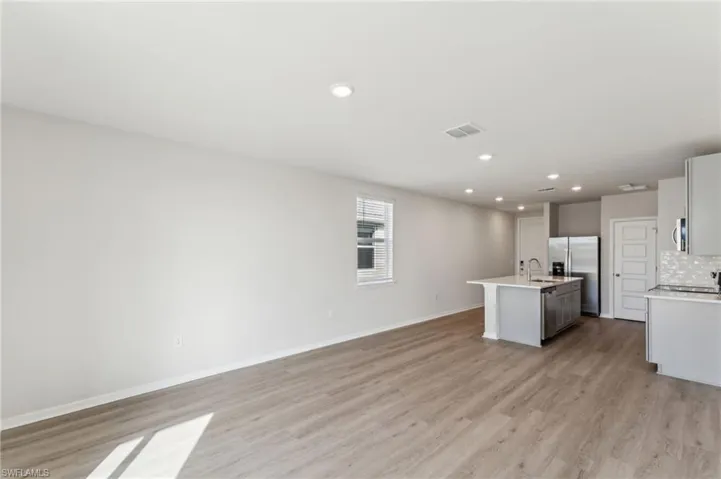 Kitchen with sink, an island with sink, stainless steel appliances, light hardwood / wood-style floors, and backsplash