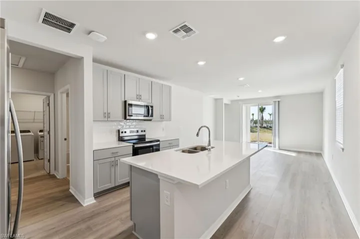 Kitchen with gray cabinets, sink, a kitchen island with sink, stainless steel appliances, and light hardwood / wood-style flooring