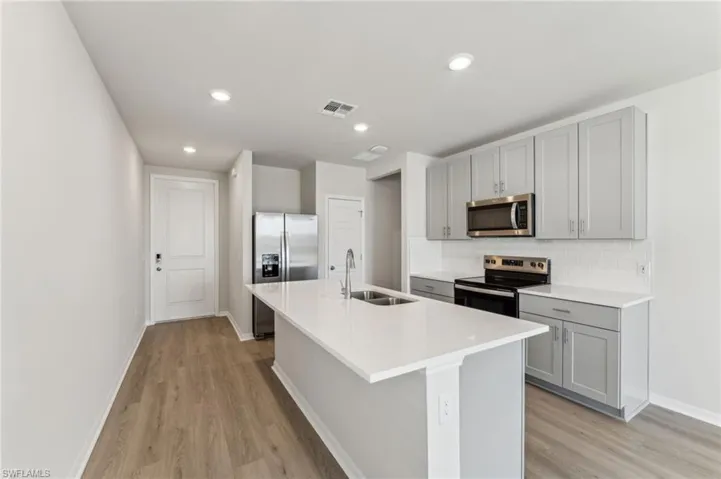 Kitchen featuring gray cabinets, appliances with stainless steel finishes, sink, backsplash, and a kitchen island with sink