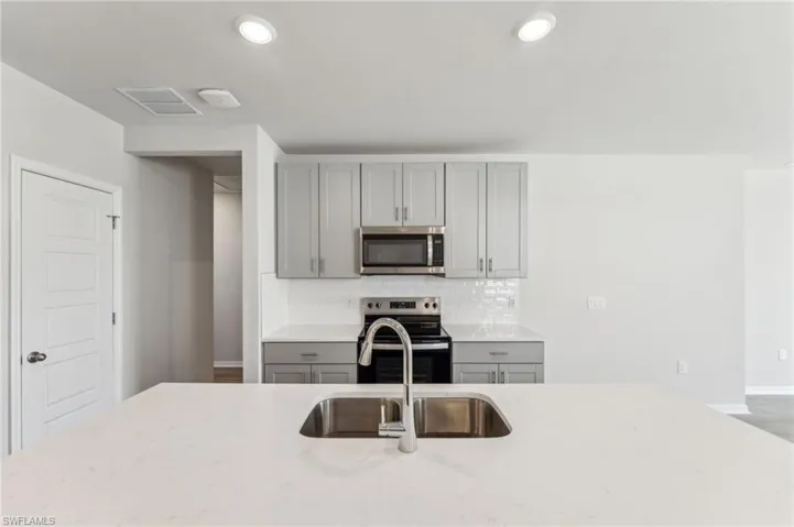 Kitchen featuring sink, appliances with stainless steel finishes, gray cabinetry, backsplash, and light stone counters