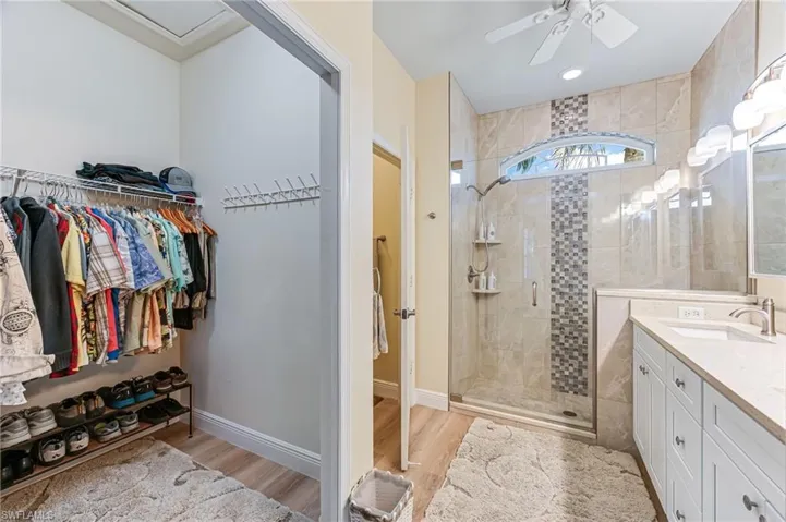 Bathroom with wood-type flooring, vanity, ceiling fan, and a shower with shower door