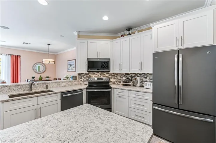 Kitchen with stainless steel appliances, white cabinetry, crown molding, and sink