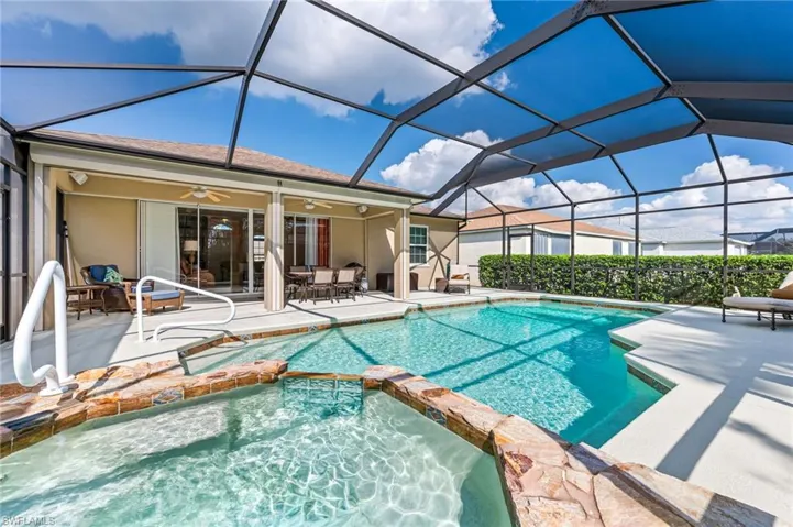 View of pool featuring ceiling fan, an in ground hot tub, a patio, and glass enclosure