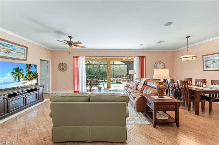 Living room featuring light wood-type flooring, ceiling fan, and ornamental molding