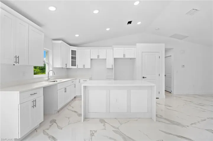 Kitchen with white cabinets, a center island, recessed lighting, light stone counters, and lofted ceiling