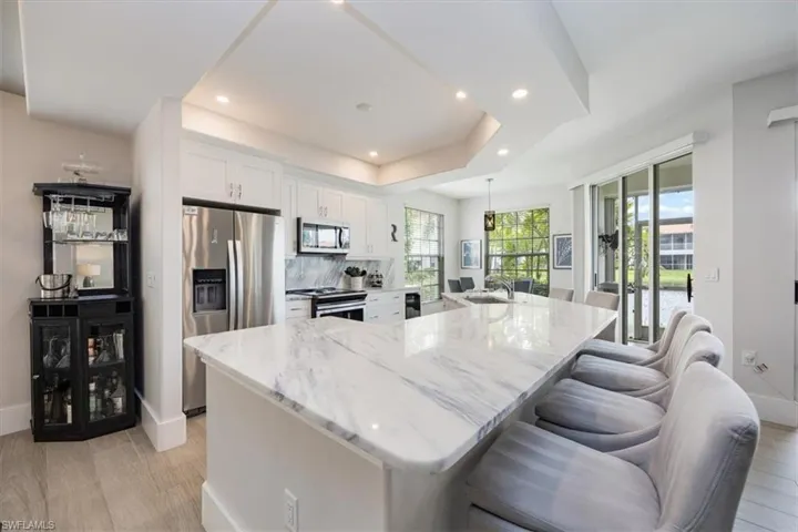 Kitchen featuring appliances with stainless steel finishes, light stone countertops, white cabinetry, a spacious island, and a breakfast bar