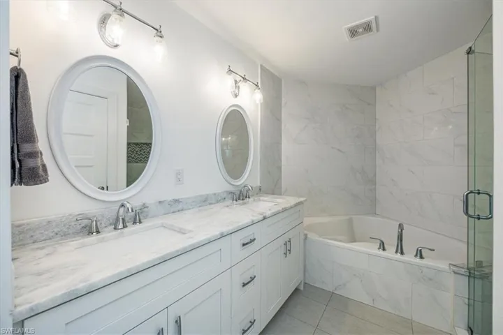 Bathroom featuring double vanity, a bath, a shower stall, and light tile patterned floors