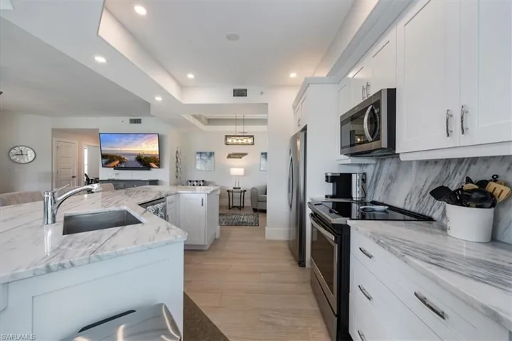 Kitchen with stainless steel appliances, white cabinetry, a raised ceiling, light wood-style flooring, and light stone countertops
