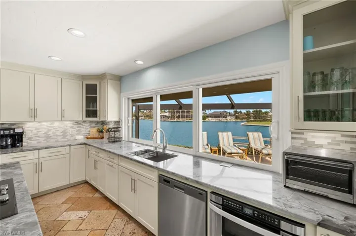 Kitchen with glass insert cabinets, decorative backsplash, light stone counters, and recessed lighting