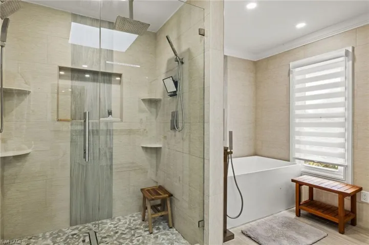 Bathroom featuring a freestanding tub, a stall shower, tile walls, and wood finished floors