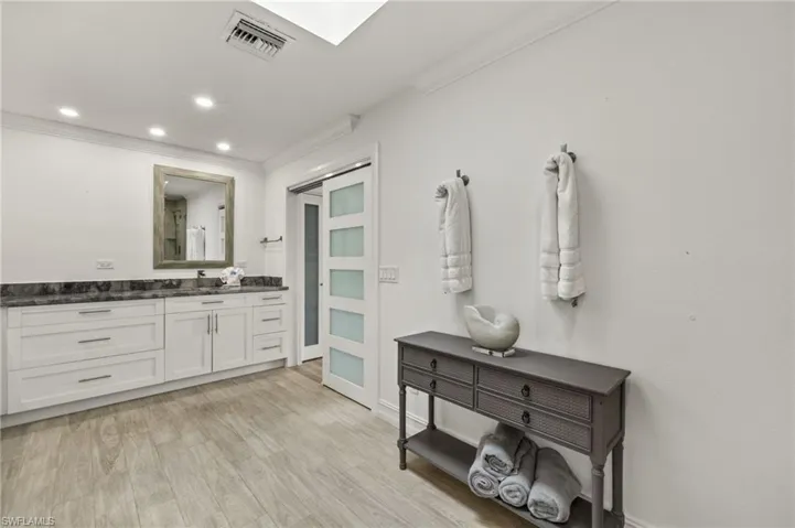Full bath with vanity, ornamental molding, recessed lighting, light wood finished floors, and a skylight