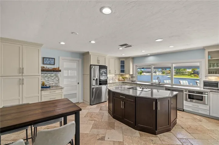 Kitchen featuring glass insert cabinets, dark stone countertops, stainless steel appliances, recessed lighting, and stone tile flooring