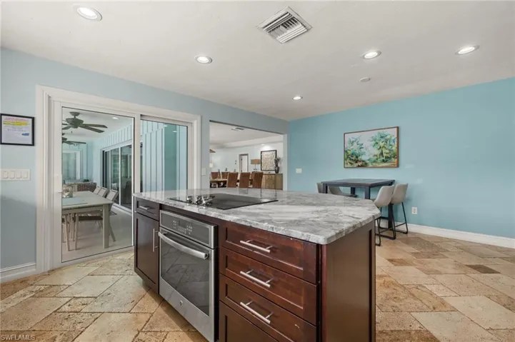Kitchen with stainless steel oven, stone tile flooring, a kitchen island, recessed lighting, and light stone counters