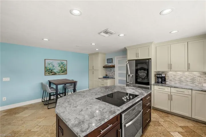 Kitchen featuring stone tile floors, light stone counters, cream cabinets, appliances with stainless steel finishes, and recessed lighting