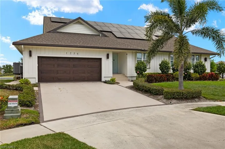 View of front of home featuring a shingled roof, driveway, roof mounted solar panels, a garage, and a front lawn