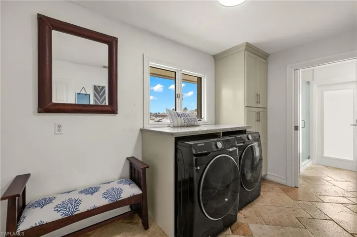 Washroom with stone tile floors, washer and dryer, and cabinet space