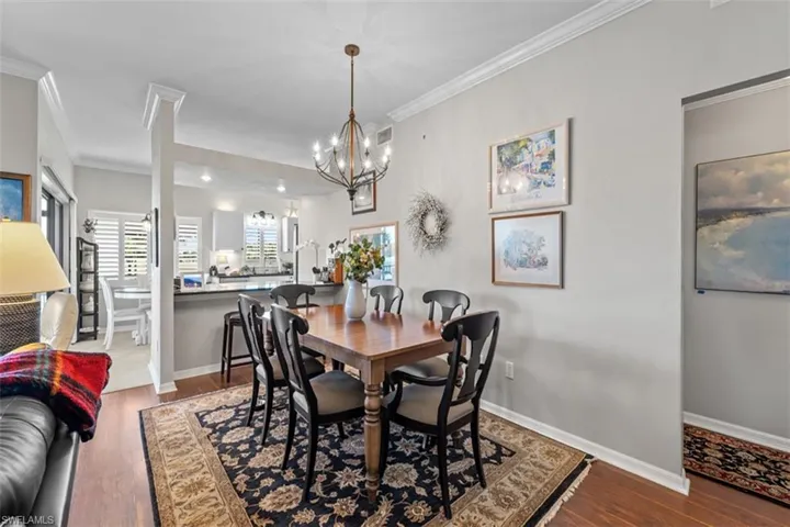 Dining area featuring wood-finish flooring, a chandelier, crown molding, and a pass-through opening to the kitchen with bar seating