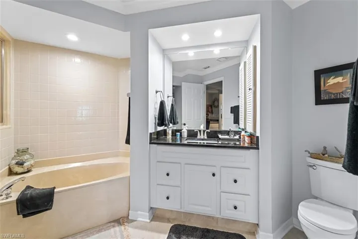Built-in soaking tub with tiled surround, accompanied by a single vanity featuring a dark countertop and ample storage cabinetry