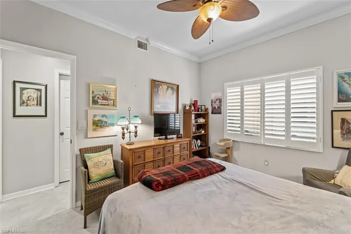 Bedroom featuring a ceiling fan with integrated lighting, crown molding, and plantation shutters