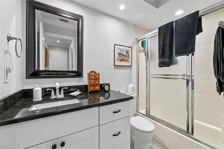 Bathroom featuring a white vanity with black hardware, a dark countertop, an undermount sink, and a framed mirror