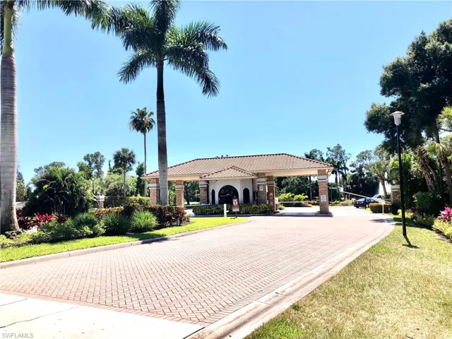Gated community entry featuring surrounded by mature palm trees and lush landscaping