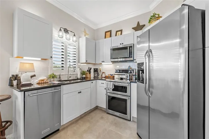 Modern kitchen featuring white shaker cabinetry, stainless steel appliances, black countertops, and a subway tile backsplash