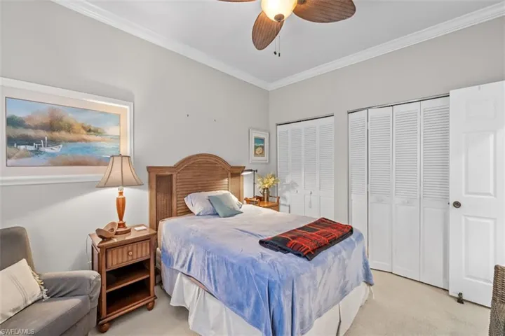 Bedroom featuring light gray walls, white crown molding, a ceiling fan with wood-finish blades, and multiple louvered bifold closet doors
