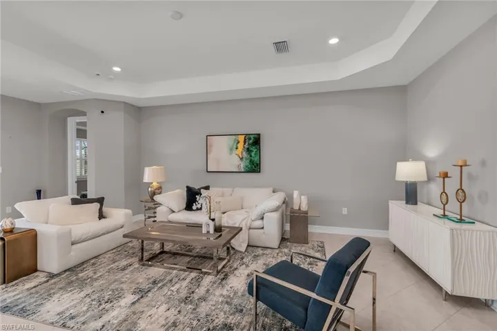 Living area with arched walkways, light tile patterned floors, a raised ceiling, visible vents, and baseboards