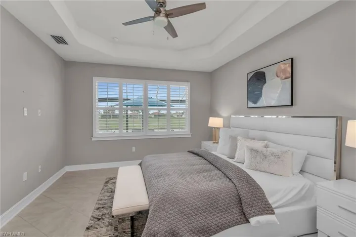 Bedroom with a tray ceiling, visible vents, a ceiling fan, light tile patterned flooring, and baseboards