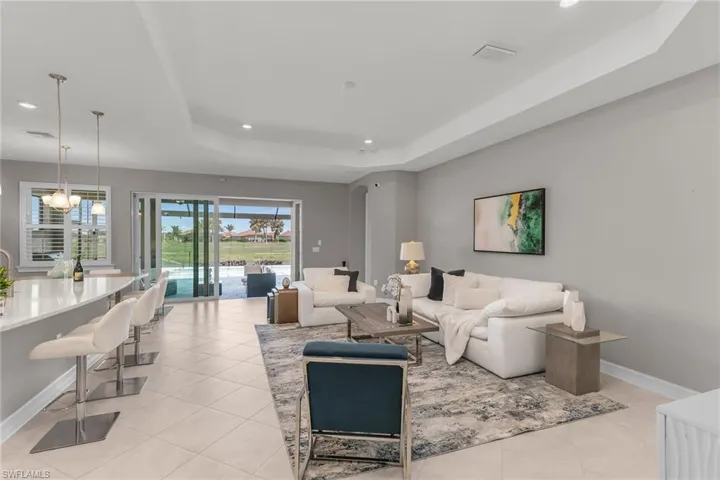 Living room with a tray ceiling, a notable chandelier, light tile patterned floors, visible vents, and baseboards