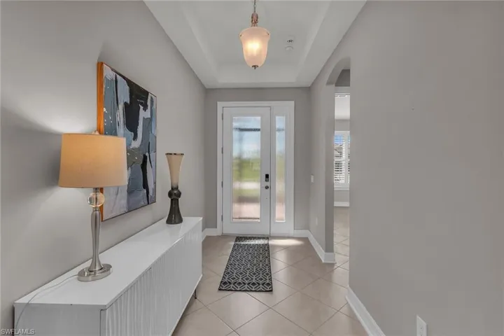 Foyer with arched walkways, light tile patterned flooring, a raised ceiling, and baseboards